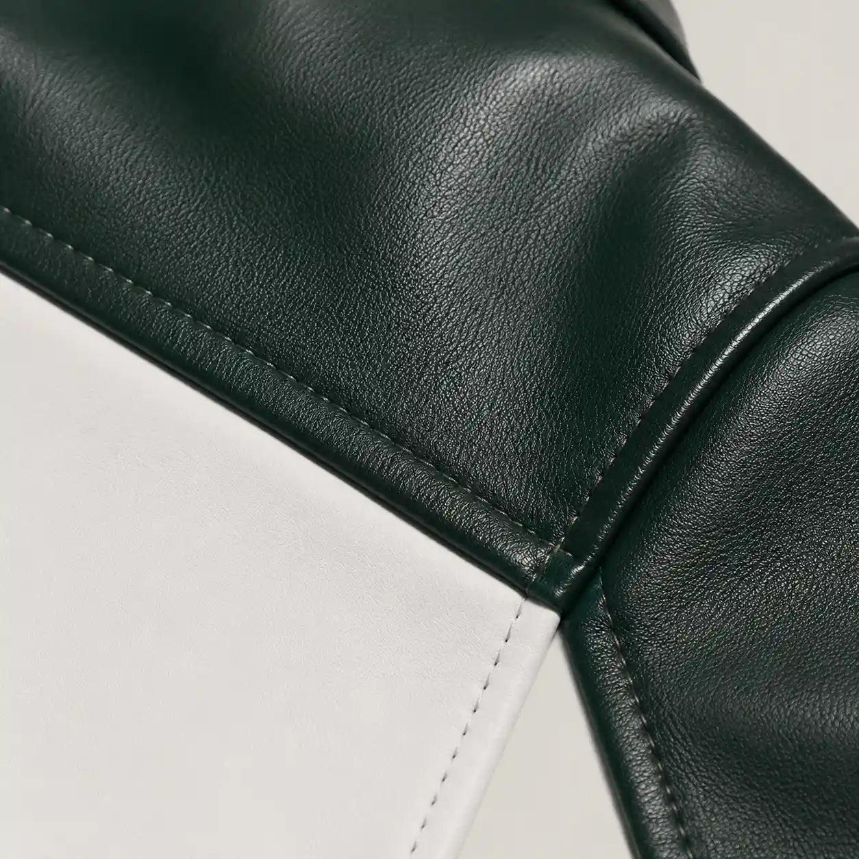 Close-up of a dark green pebbled leather material meeting a white leather panel, showing clean stitching and a curved seam.