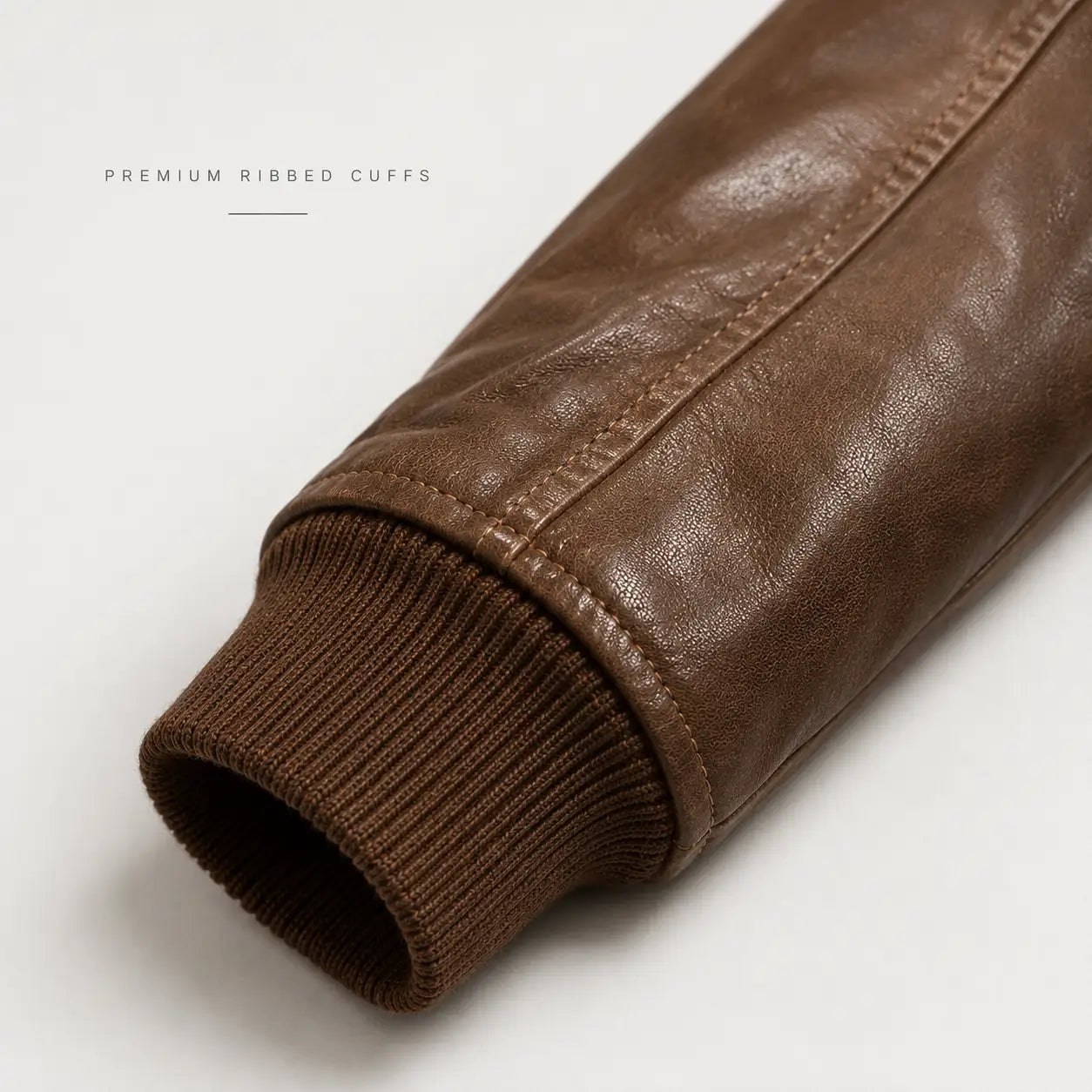 Close-up of a brown leather sleeve with a ribbed knit cuff, shown on a light gray background with the text 'PREMIUM RIBBED CUFFS' in the upper left.