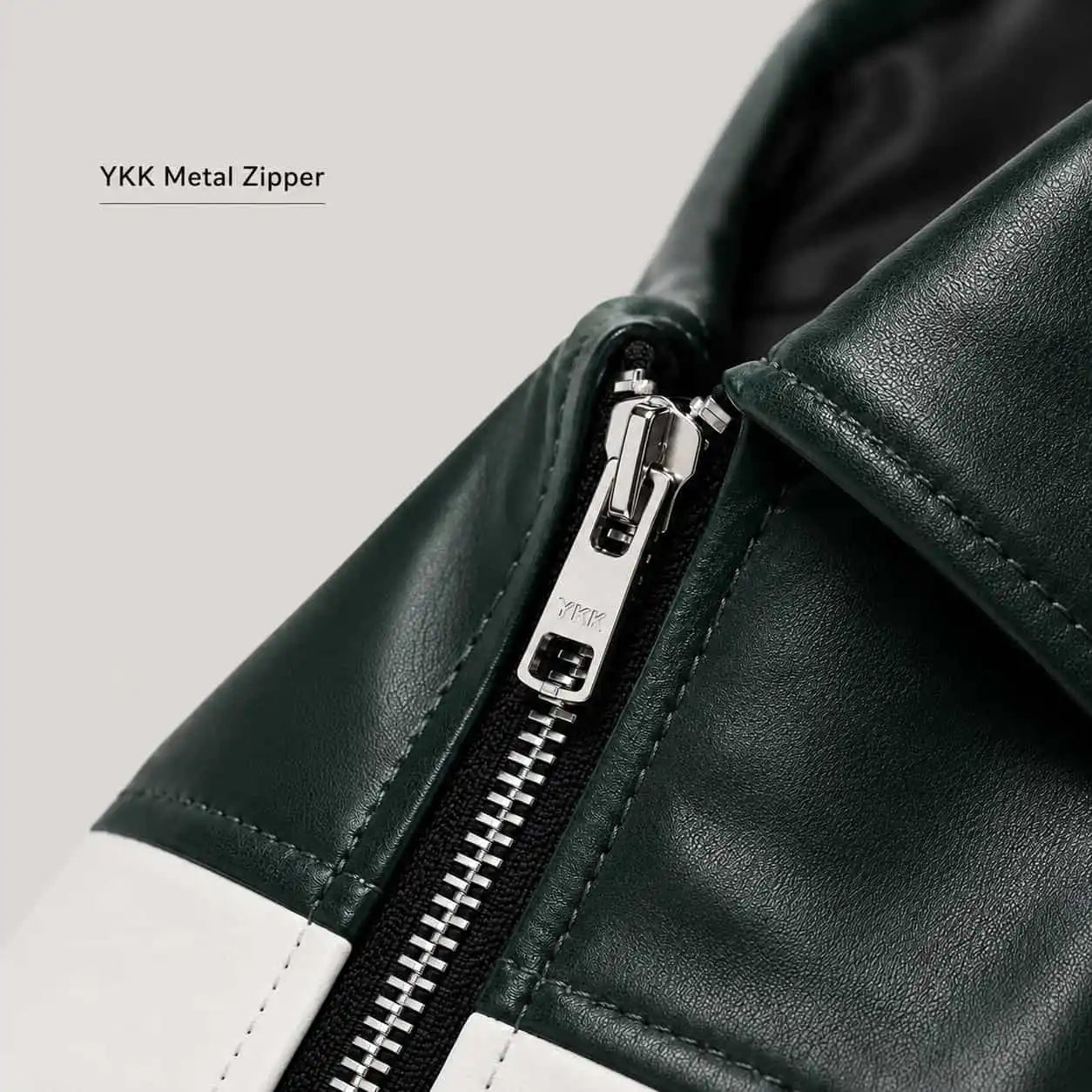 Close-up of a dark green leather jacket with a white contrast panel and a silver YKK metal zipper, featuring a text overlay 'YKK Metal Zipper' on a light gray background.